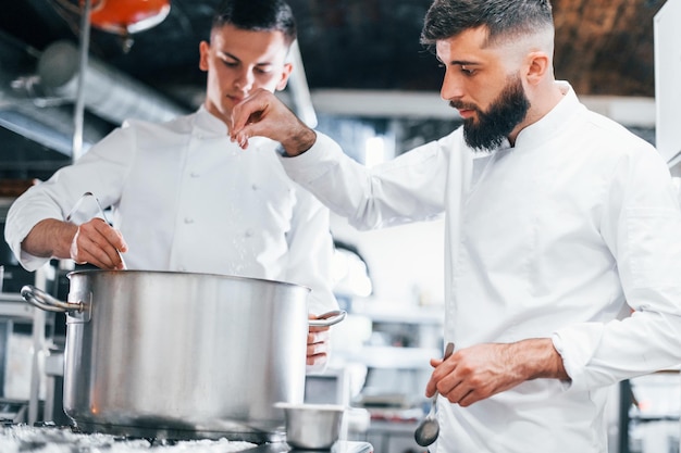 Con la ayuda de otro empleado Chef en uniforme blanco cocinando comida en la cocina Día ajetreado en el trabajo