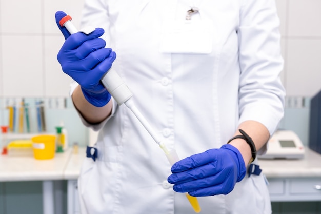 Ayudante de laboratorio con una pipeta en sus manos para análisis de sangre
