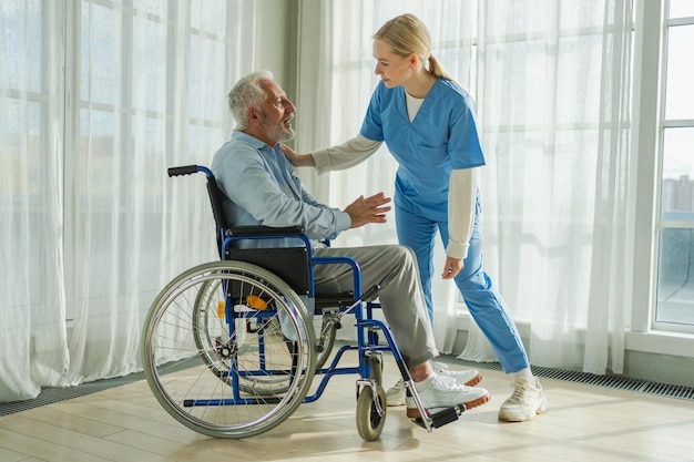 Ayudar a apoyar la jubilación de la atención médica enfermera que ayuda al anciano en silla de ruedas paciente y la mujer en la enfermería