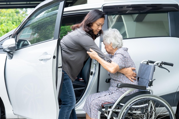 Ayudar y apoyar a la paciente asiática mayor o anciana sentada en una silla de ruedas, prepararse para llegar a su automóvil, concepto médico fuerte y saludable.
