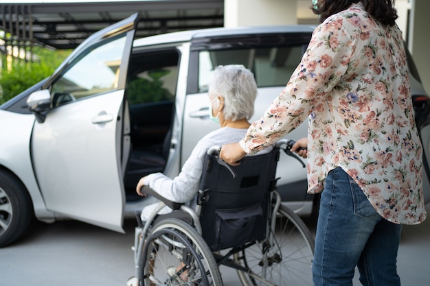 Ayudar y apoyar paciente mujer mayor asiática sentada en silla de ruedas prepararse para llegar a su coche