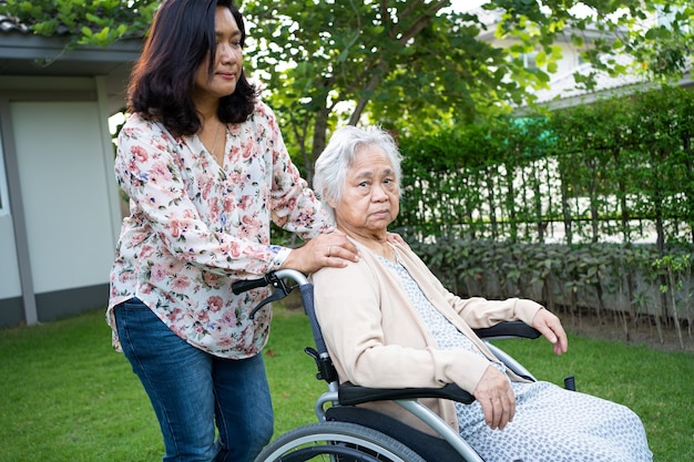 Ayude a una anciana asiática mayor o anciana en silla de ruedas eléctrica y con una mascarilla para proteger la infección de seguridad Covid 19 Coronavirus en el parque