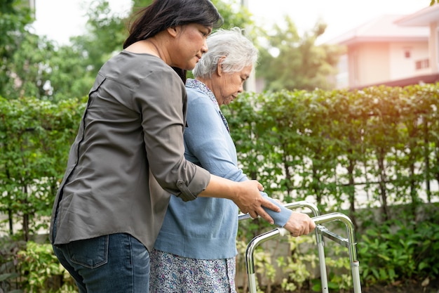 Ayude y cuide a la anciana asiática mayor o anciana que use el andador con una salud fuerte mientras camina en el parque en felices vacaciones frescas.