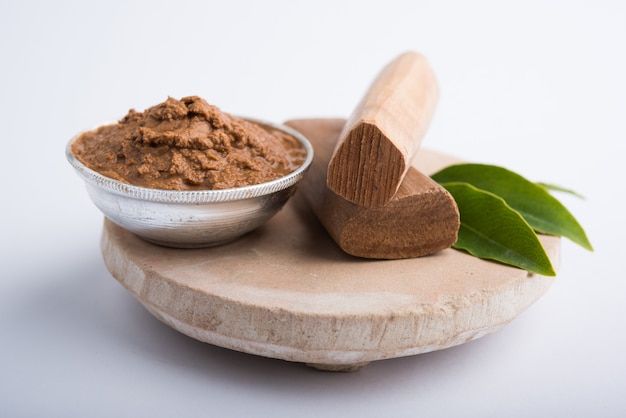 Ayurvedische Chandan- oder Sandelholzpaste in Silberschale mit Stäbchensandblättern über Sahanor Sahana oder rundem Steinsockel zur Herstellung von Paste