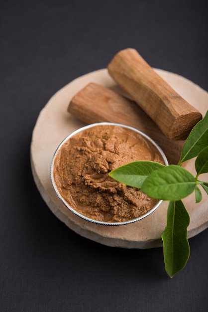 Ayurvedische Chandan- oder Sandelholzpaste in Silberschale mit Stäbchensandblättern über Sahanor Sahana oder rundem Steinsockel zur Herstellung von Paste