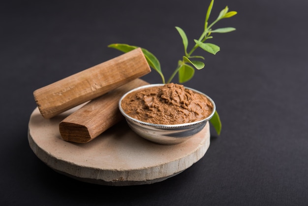 Ayurvedische Chandan- oder Sandelholzpaste in Silberschale mit Stäbchensandblättern über Sahanor Sahana oder rundem Steinsockel zur Herstellung von Paste