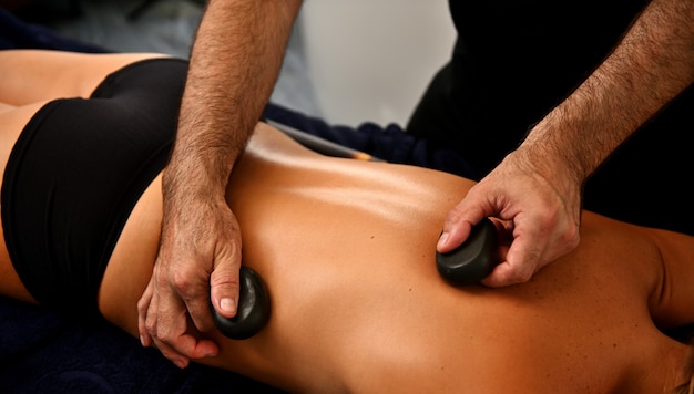 Ayurvedische Hot-Stone-Massage im modernen Spa-Salon. Körperpflegekonzept. Masseur massiert den Rücken einer Frau mit Lavasteinen