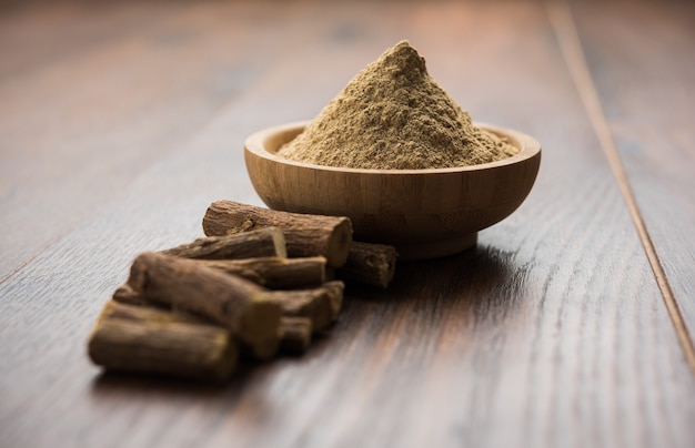 Ayurvedisches Mulethi- oder Süßholzwurzel-Stick oder Jeshtamadh-Pulver, serviert in einer Schüssel auf stimmungsvollem Hintergrund