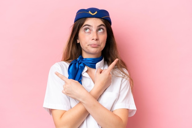 Foto azafata de avión mujer caucásica aislada sobre fondo rosa apuntando a los laterales que tienen dudas