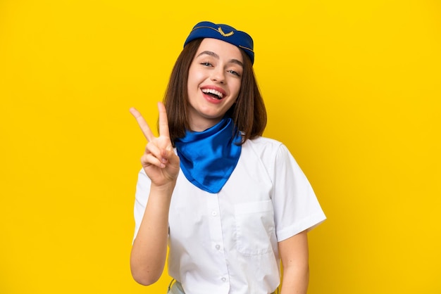 Azafata de avión mujer ucraniana aislada de fondo amarillo sonriendo y mostrando el signo de la victoria