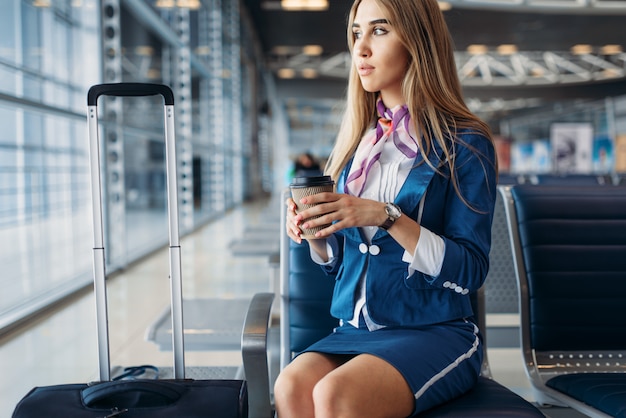 Azafata con café en el asiento en la zona de espera