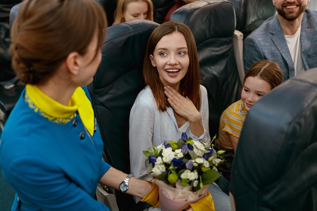Azafata dando flores a mujer alegre en avión