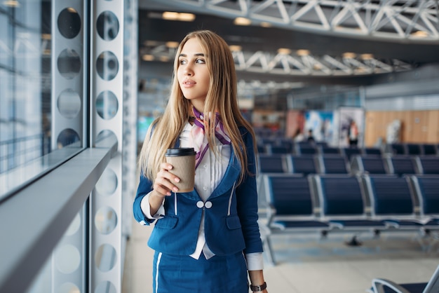 Azafata con equipaje de mano y café en el aeropuerto