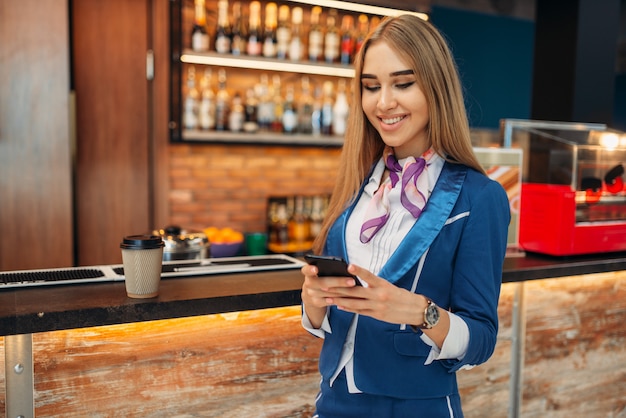 Azafata mediante teléfono móvil en la cafetería del aeropuerto