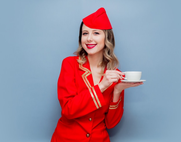 Azafata vestida con uniforme rojo con taza de café o te