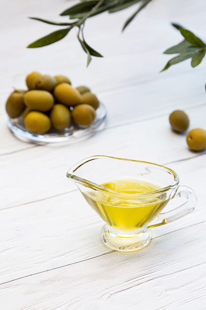 Azeite e tigela de azeitonas verdes em uma mesa de madeira branca