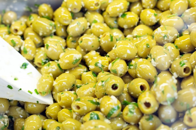 Azeitonas verdes com alho e ervas no balcão com colher para venda no mercado.