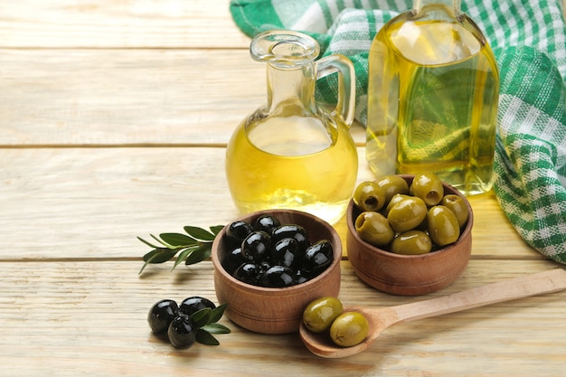 Azeitonas verdes e pretas em uma tigela de madeira com folhas e azeite de oliva em uma mesa de madeira natural