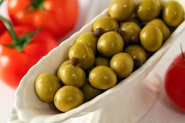 Azeitonas verdes em pratos decorativos com tomates vermelhos sobre fundo branco, grande formato