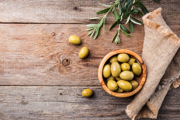 Azeitonas verdes frescas em uma tigela e ramo de oliveira em madeira rústica