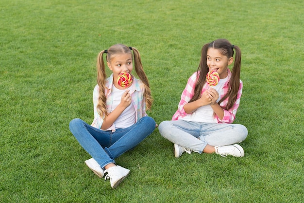 Azúcar y calorías. Amigos alegres alegres comiendo dulces al aire libre. Comida de vacaciones. Confitería. Caramelo dulce. Los niños felices sostienen la hierba del asiento del caramelo. Dulcería. Golosinas de piruleta. Candy significa felicidad.