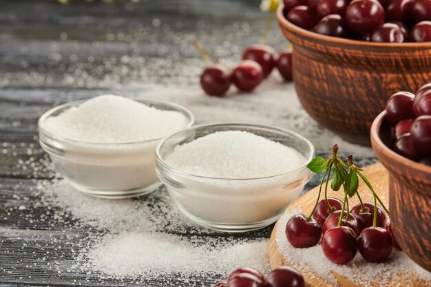 Azúcar para conservar en tazones sobre una mesa de madera cerezas maduras sobre la mesa
