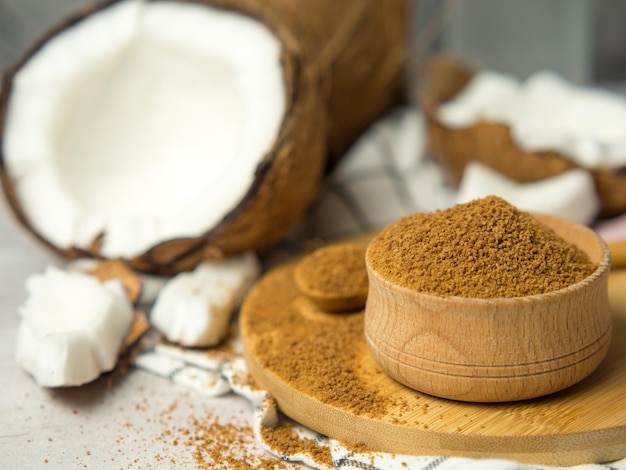 Azúcar moreno de palma de coco en un tazón de madera y una cuchara y la mitad de la fruta de coco sobre un fondo de hormigón gris