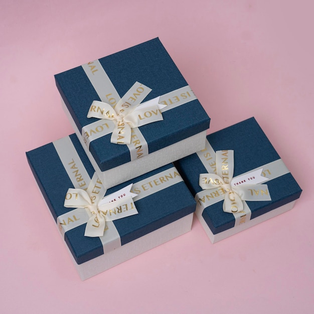 azul e dourado três caixas de presente com um laço de prata e fundo rosa isolado