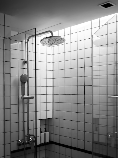 Azulejos de rejilla en blanco y negro en el interior de la moderna caja de espacio de ducha en el baño con ducha de lluvia en la partición de la puerta de vidrio de estilo vertical