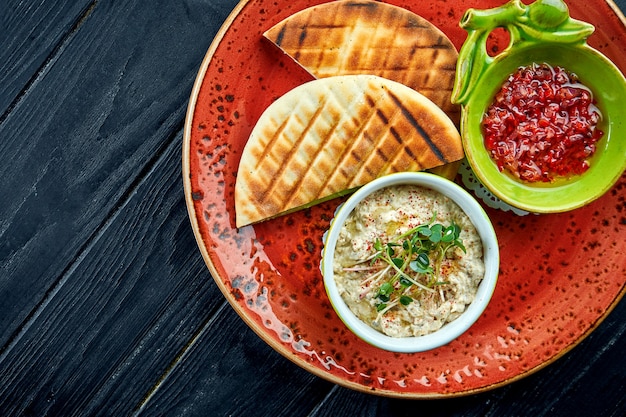 Baba ghanoush tradicional israelense ou oriental com molho de vegetais e pita, servido em um prato vermelho na mesa de madeira