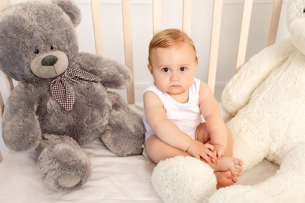 Baby 1 Jahr alt sitzt in einem Kinderbett mit großen Teddybären, Baby im Kinderzimmer
