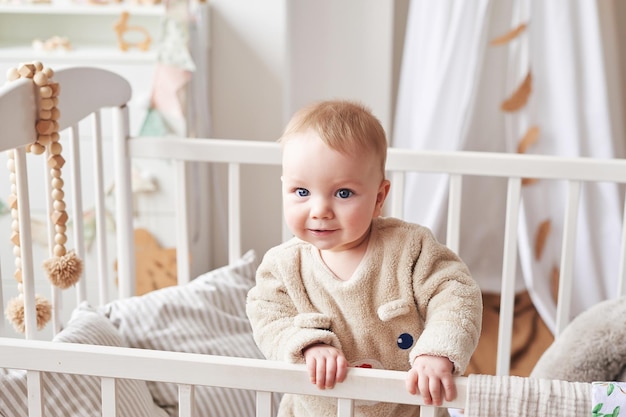 Baby 6 Monate stehen im Kinderbett im Kinderzimmer. Glückliche Mutterschaft und Vaterschaft. Entbindungsheim und Klinik. Vater- und Muttertag. Frühkindliche Entwicklung, Kindergarten