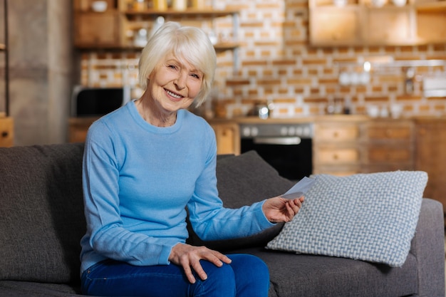 Baby boomer. Mulher idosa encantada segurando um bilhete e sorrindo enquanto está de bom humor