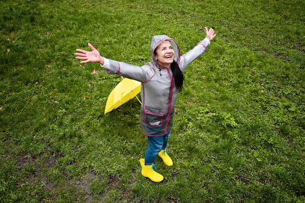 Baby boomers e saúde mental feliz mulher sênior em capa de chuva amarela com guarda-chuva amarelo pulando