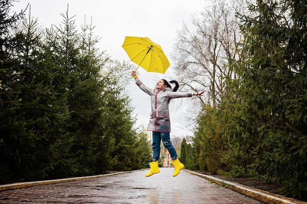 Baby boomers y mujer mayor feliz de salud mental en impermeable amarillo con paraguas amarillo saltando