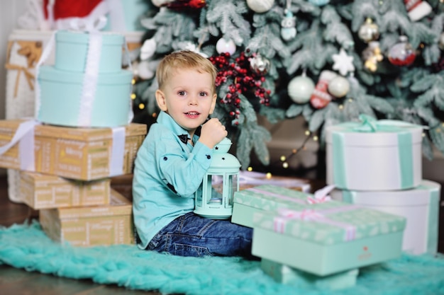 Baby Boy abre cajas con regalos debajo del árbol de Navidad y sonríe