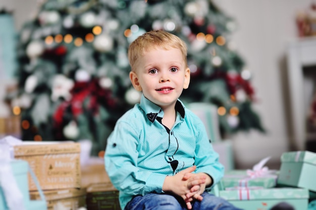 Baby Boy abre cajas con regalos debajo del árbol de Navidad y sonríe