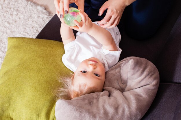 Baby Boy Blick in die Kamera auf Kissen legen, kleinen Ball in seinen Armen halten.