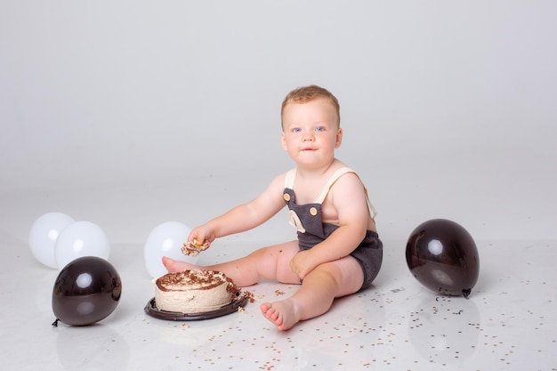 Baby Boy celebra cumpleaños con globos y tarta sobre fondo blanco.