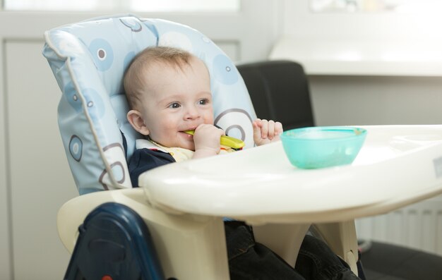 Baby Boy emplazamiento en trona en la cocina y comiendo