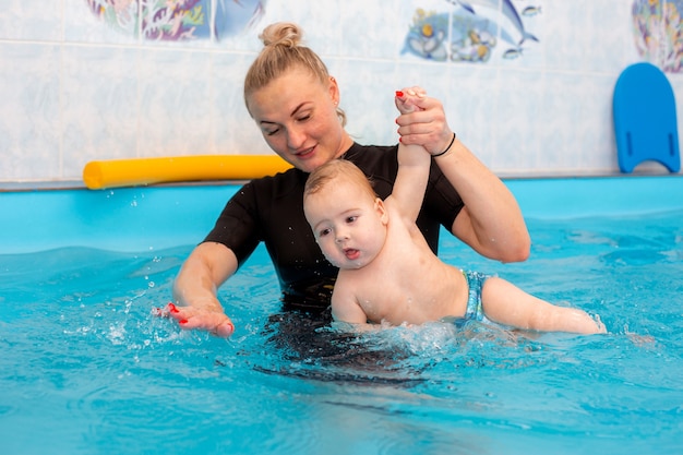 Baby Boy entrena para nadar en la piscina con un entrenador