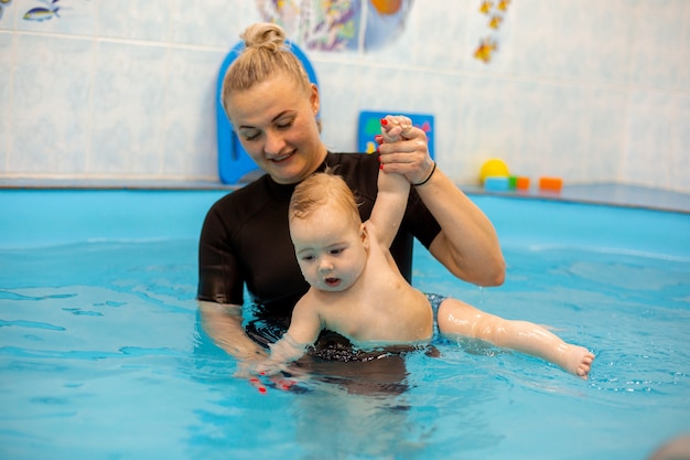 Baby Boy entrena para nadar en la piscina con un entrenador