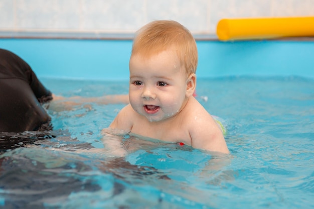 Baby Boy entrena para nadar en la piscina con un entrenador