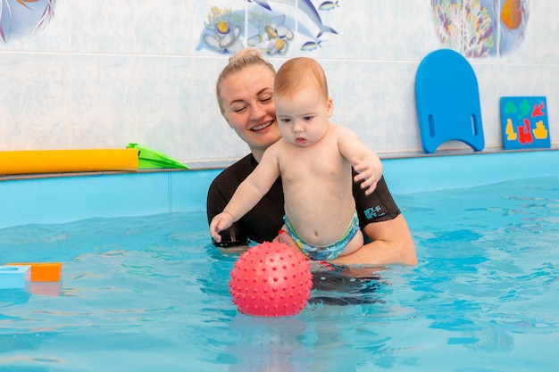 Baby Boy entrena para nadar en la piscina con un entrenador