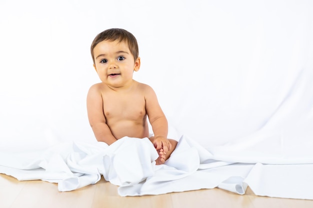 Baby Boy en un estudio con un fondo blanco, recién nacido caucásico de ocho meses sentado, jugando con un paño