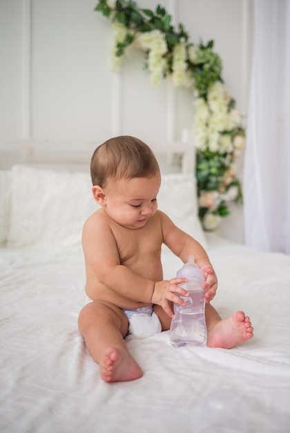 Baby Boy en un pañal sentado en la cama con una botella de agua