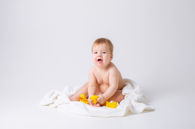 Baby Boy en un pañal sentado sobre un fondo blanco con una toalla y patos de goma concepto de baño