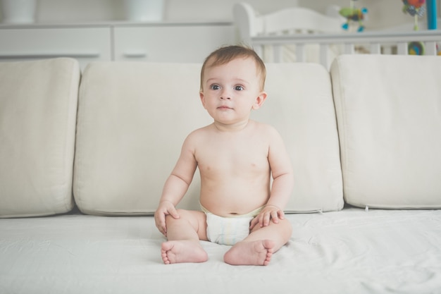 Baby Boy en pañales sentado en el sofá en el salón