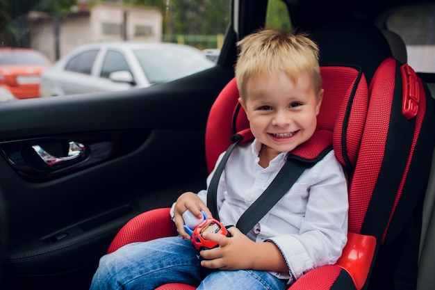 Baby Boy con el pelo rizado sentado en el asiento infantil con coche de juguete en las manos