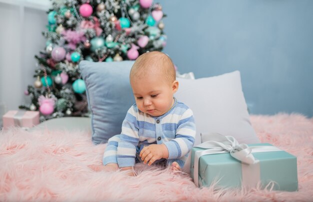 Baby Boy en pijama sentado sobre una manta de piel con un regalo con árbol de Navidad